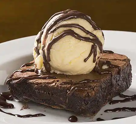 Teller mit Brownie und Schokopulver an Vanilleeis mit Schokosauce.