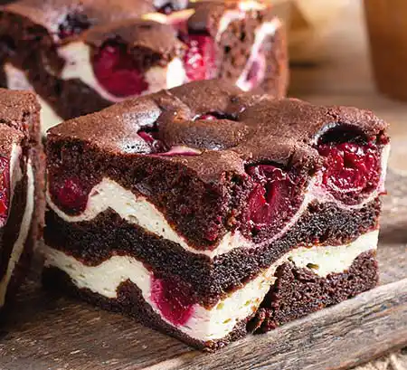 Holbrett mit Cheescake-Brownie und Kirschen.