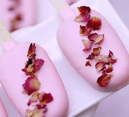 Rosafarbene Cakesicles mit getrockneter Blütendeko.