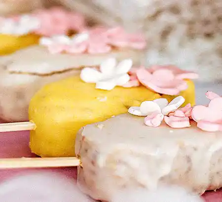Bunte Cakesicles mit farbiger Vanilleglasur und essbaren Blumen.