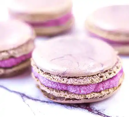 Helle Macarons mit pinkfarbener Füllung auf Marmortisch.