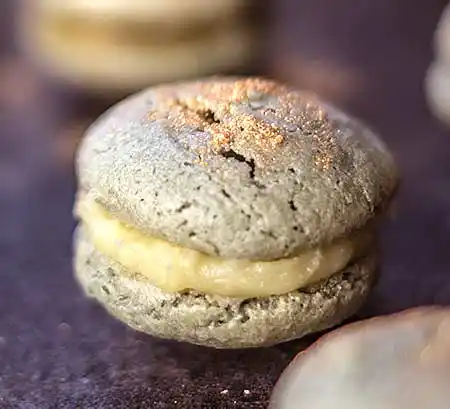 Grünlicher Macaron auf Holztisch mit Goldstaub.