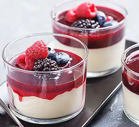 Gläser mit Panna Cotta aus gekochter Sahne mit Früchte-Ragout und frischen Beeren.