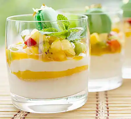 Gläser mit Joghurt-Dessert mit Mango-Kiwi-Kompott und Minzgarnitur.