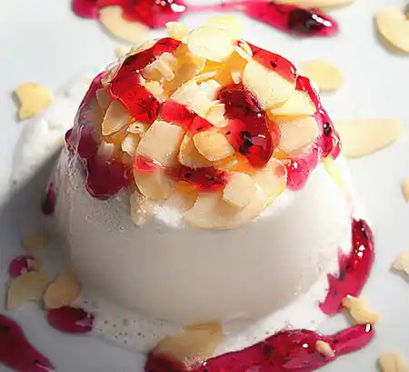 Teller mit frisch gestürzte Panna Cotta mit gehobelten Mandeln und frischem Beerenspiegel.