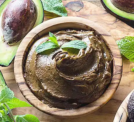 Holzschale mit Schokomousse mit Avocado-Pürree, dunkler gehobelter Schokolade und Minzgarnitur.