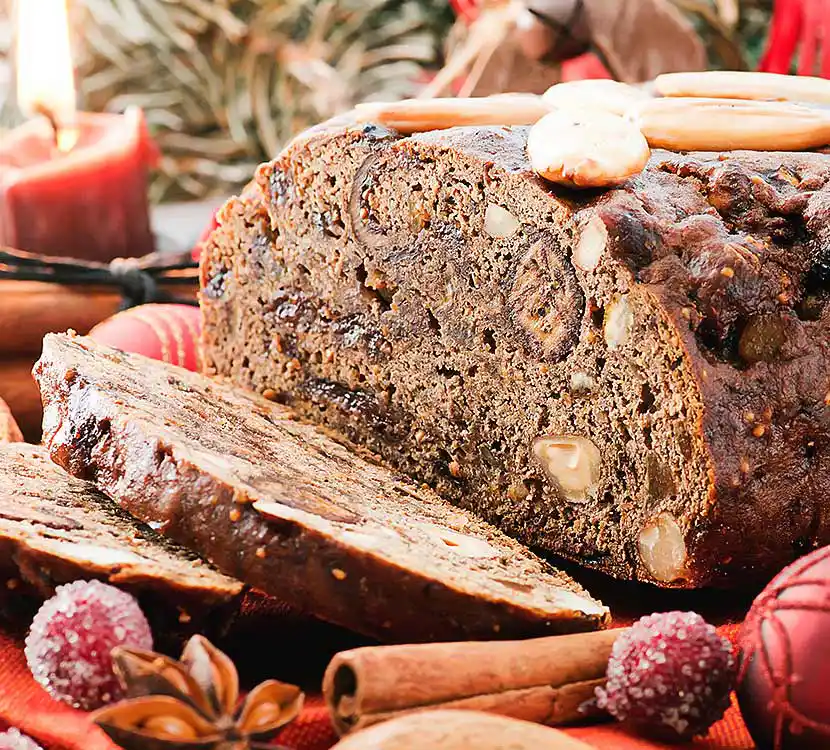 Angeschnittenes Früchtebrot auf Tischdecke mit Dekoration.