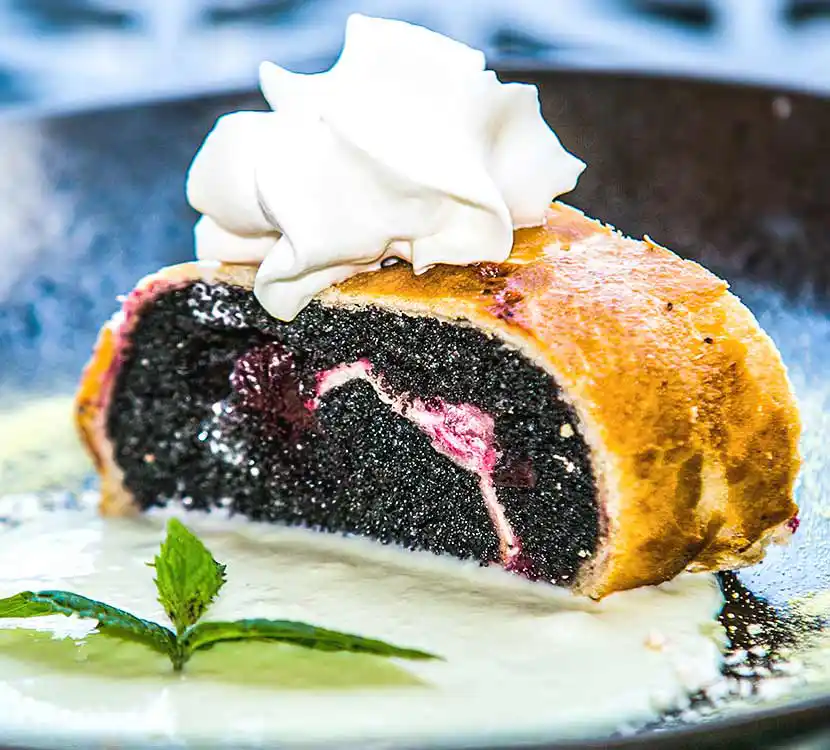 Teller mit Mohn-Cheescake-Strudel und Schlagsahne auf Teller.