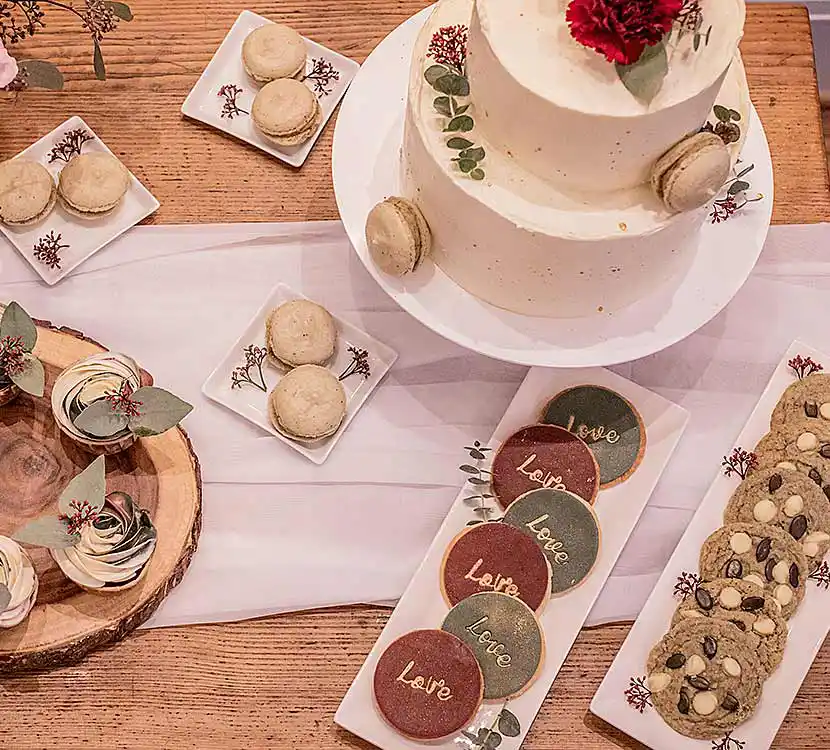 Holztisch mit Hochzeitstorte, Cupcakes und Cookies auf Teller.