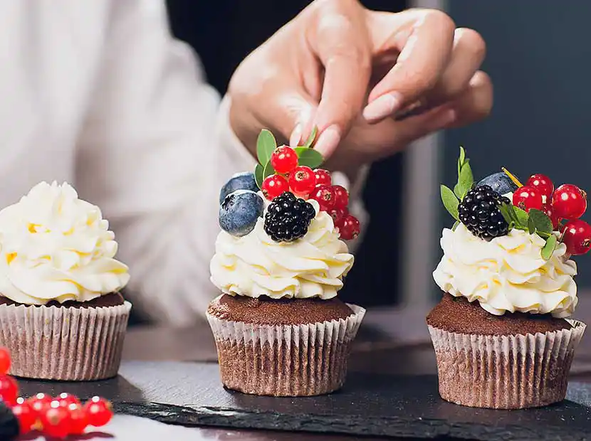 Konditorinnenhände verzieren mit Beeren Muffin-Toppings.