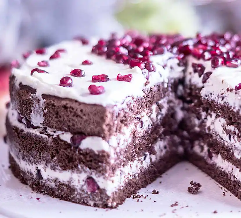 Angeschnittener Schokokuchen mit einer Sahnecreme-Schichtfüllung und Granatapfelkernen.