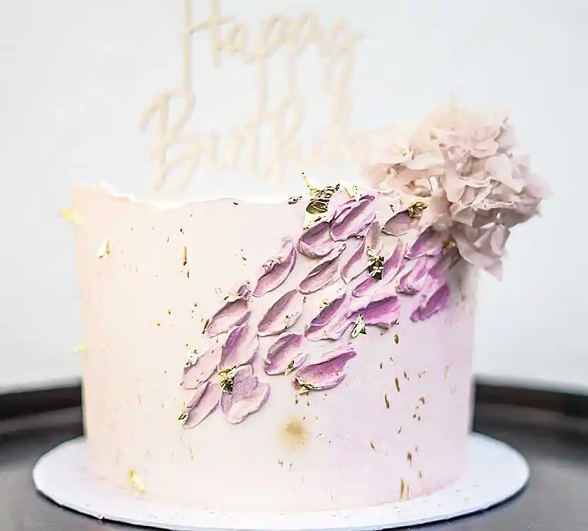 Weiße Geburtstagstorte mit farbiger Buttercreme-Struktur und Blumendeko.