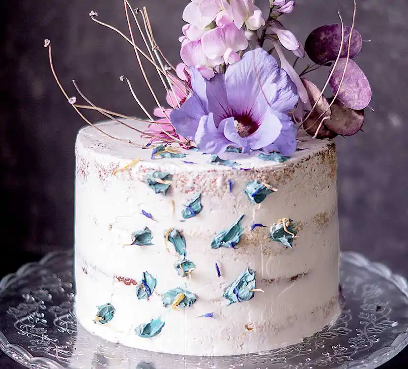 Teller mit weißer Semi Naked Torte und violettem Blumendekor.