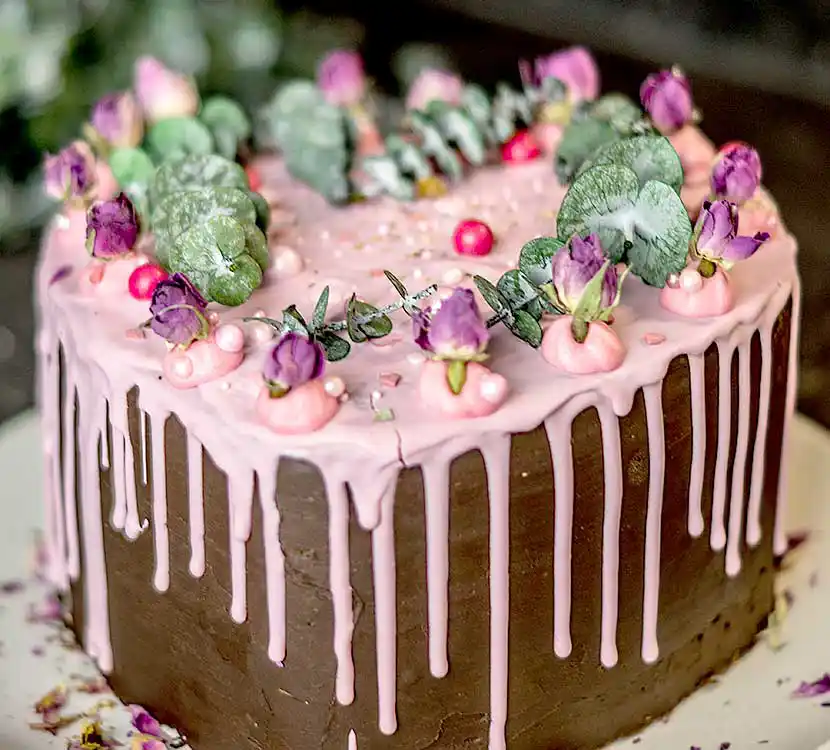 Dunkle Torte mit rosa Schoko-Drip und Zuckerguss-Kunst.