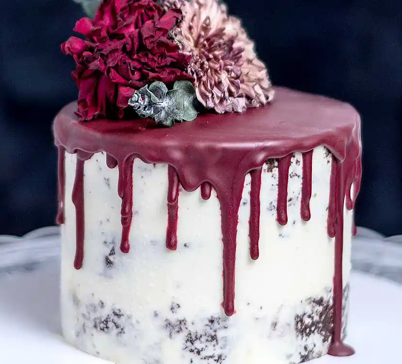 Teller mit weißer Semi Naked Torte roter Schokoladen-Drip und Blumendeko.